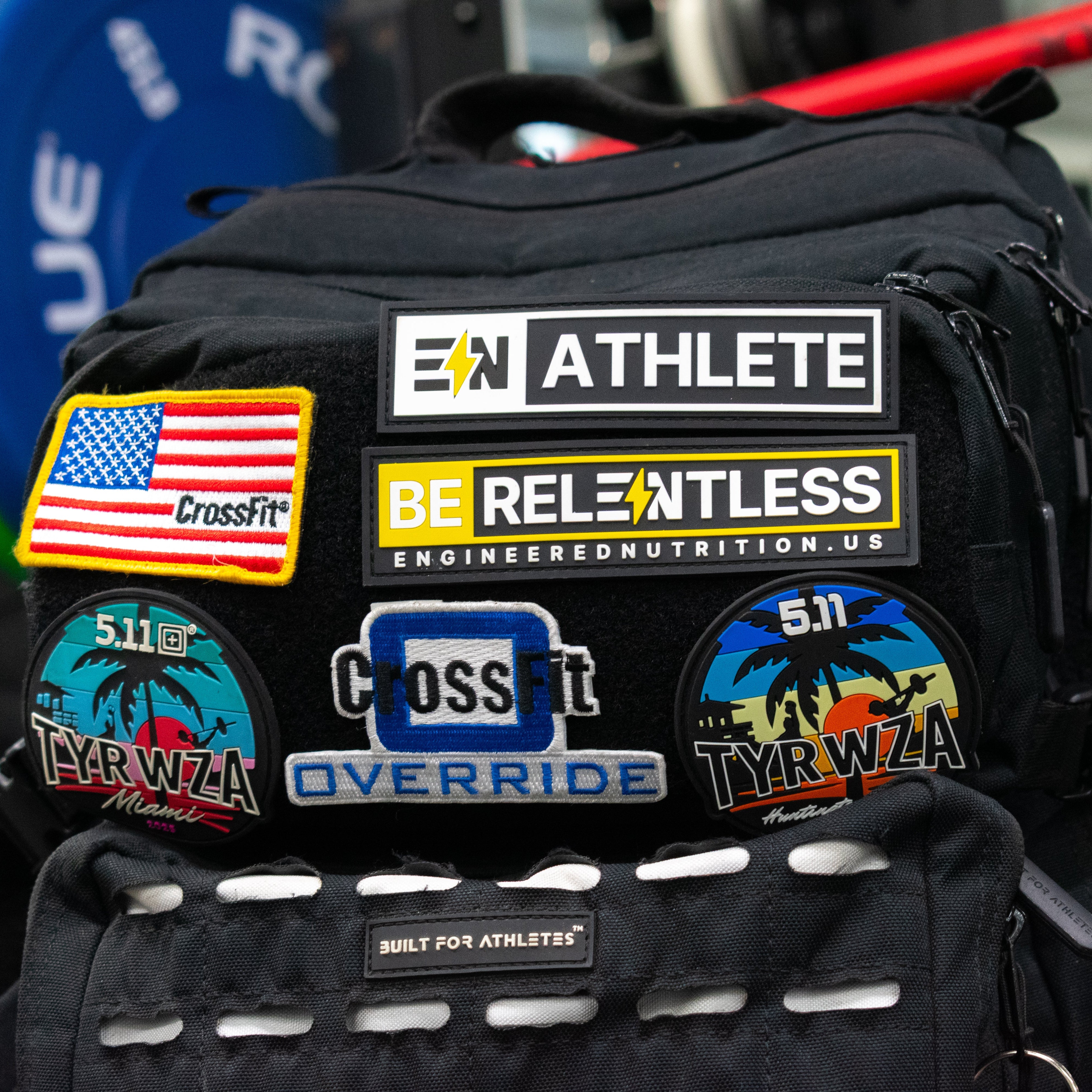 Black backpack with various patches including an American flag, CrossFit logo, and branded labels.
