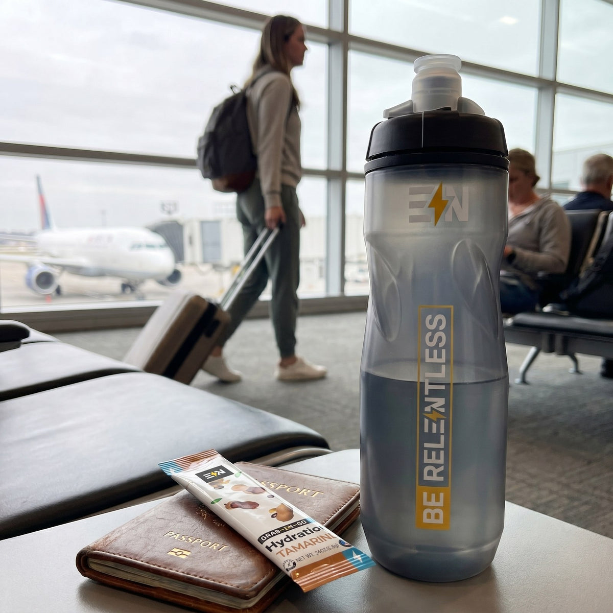 Engineered Nutrition squeeze bottle and Tamarind hydration stick on an airport gate seat with a plane at the jet bridge behind